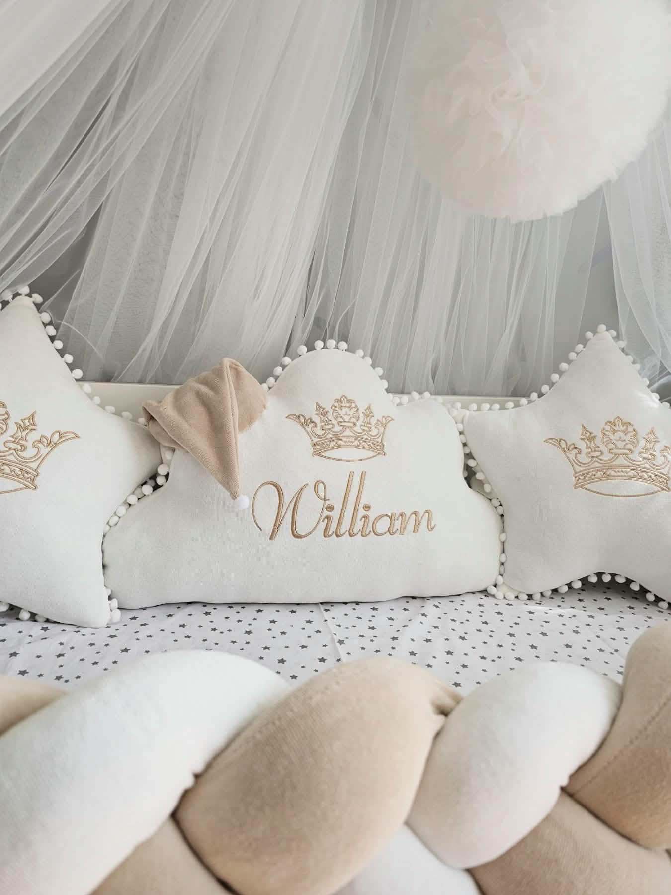 Decorative pillows with 'William' and crowns on a soft surface with tulle in the background.