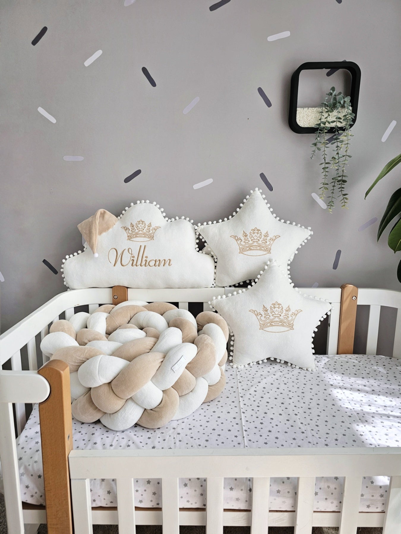 Nursery crib with decorative pillows and a braided rope toy against a gray wall with white polka dots.