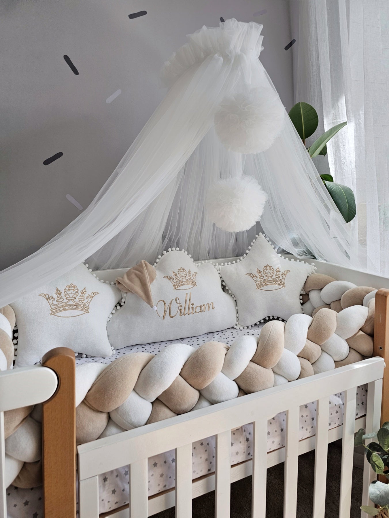 Nursery crib with decorative pillows and canopy in a well-lit room.