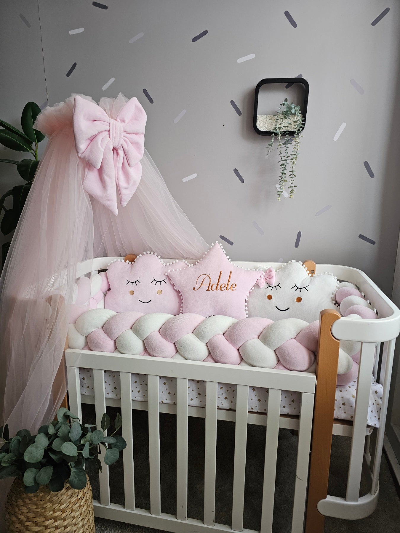 Baby crib with decorative pillows and a pink canopy in a nursery setting.