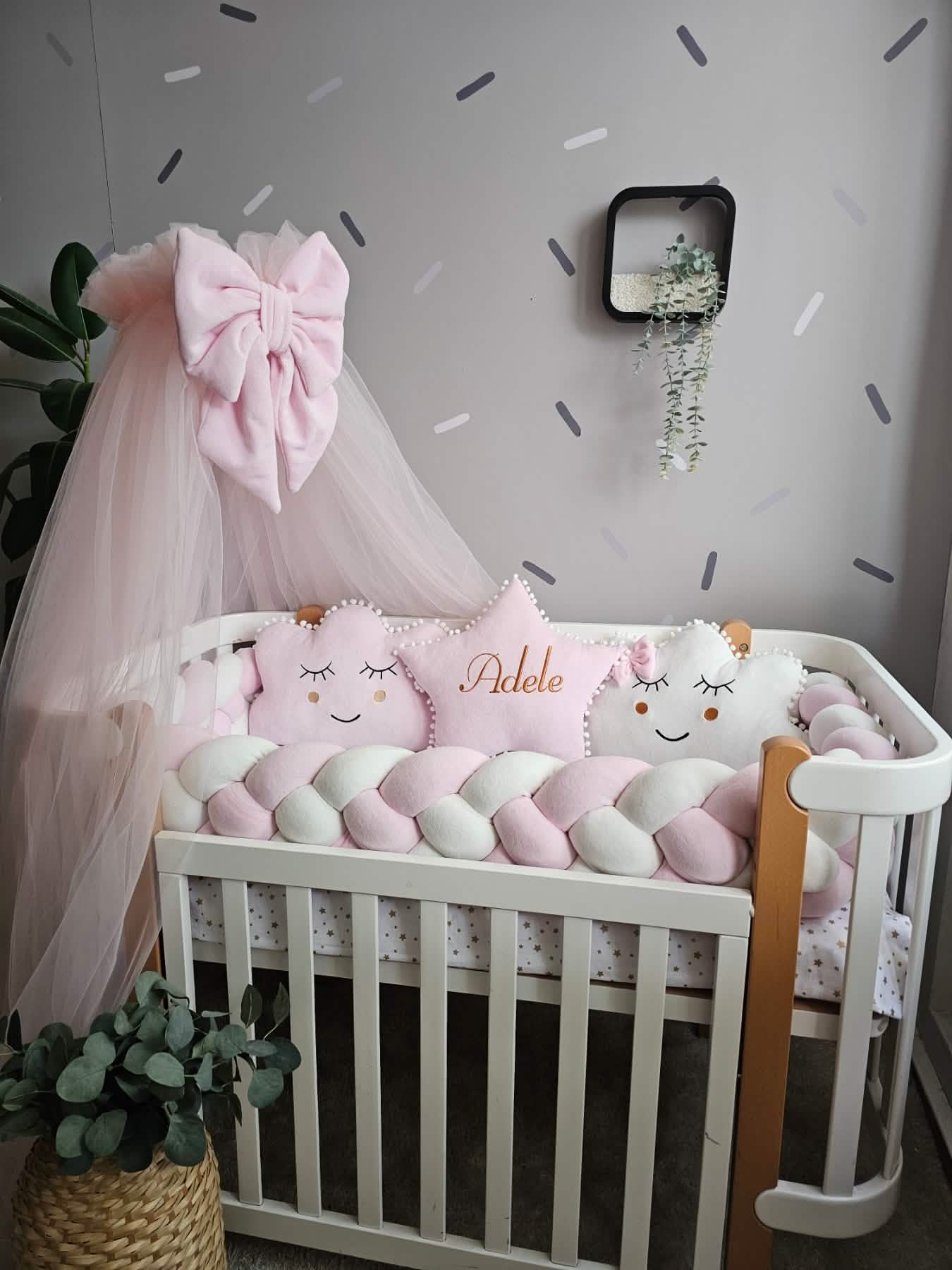Baby crib with decorative pillows and a pink canopy in a nursery setting.