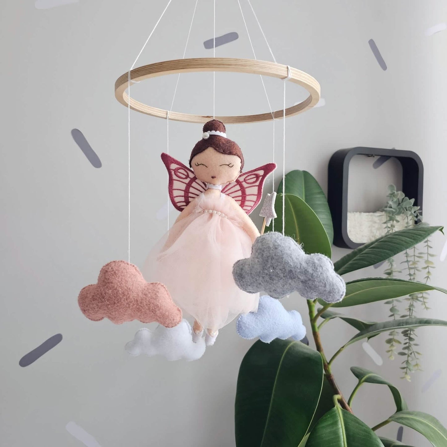 Fairy doll mobile with clouds hanging from a wooden ring against a light gray wall.