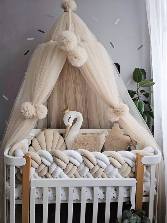 Baby crib with decorative canopy, pom-poms, and swan pillow in a nursery setting.