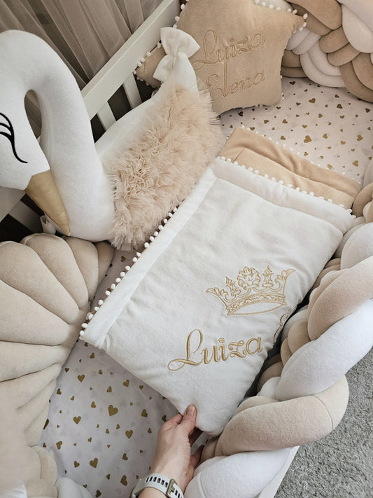 Baby crib with decorative pillows and a blanket featuring the name 'Luiza' and a crown design.