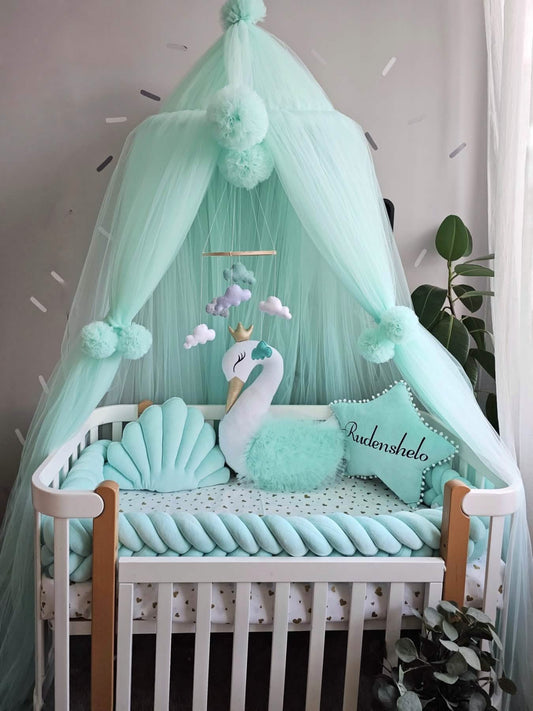 Children's crib with mint green bedding, canopy, and decorative elements in a room.