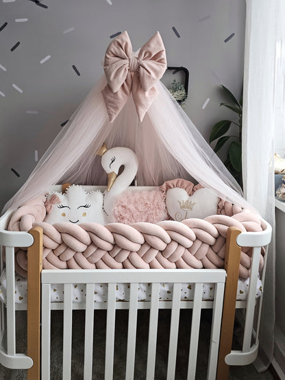 Children's crib with pink bedding, swan pillow, and decorative bow in a room with gray walls and white trim.