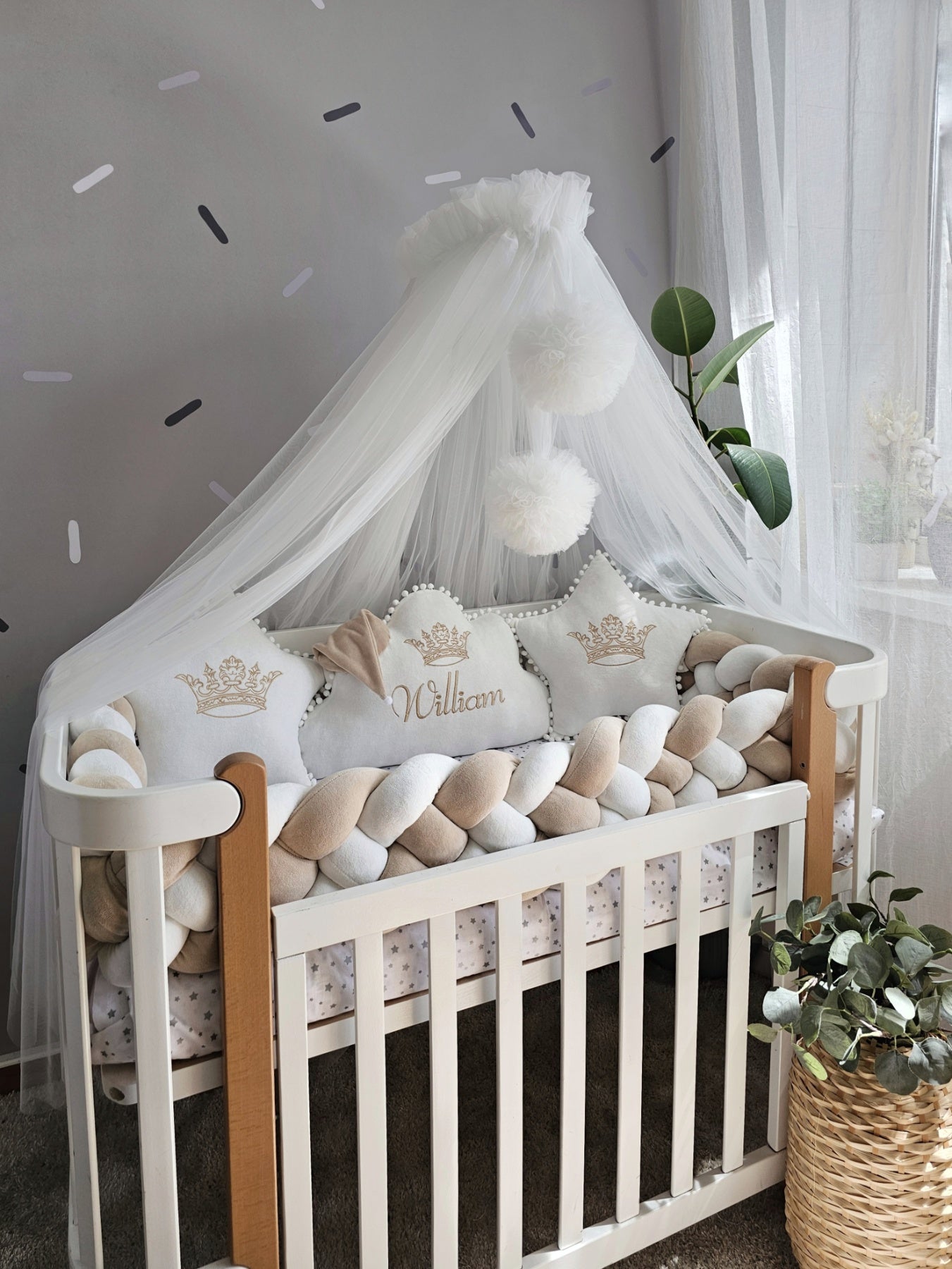 Baby crib with white bedding, decorative pillows, and a canopy in a nursery setting.