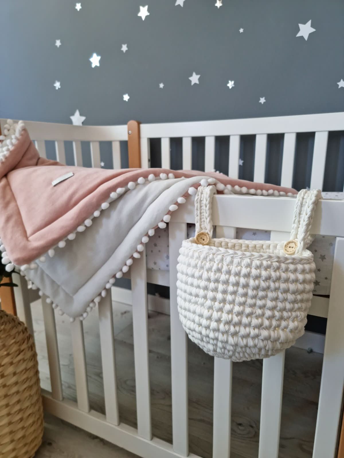 Nursery with white crib, pink blanket, and woven basket against a star-patterned wall.