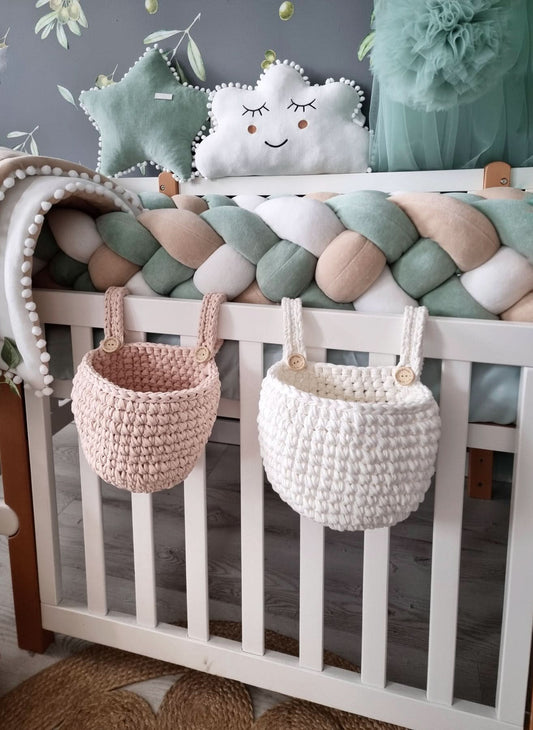Crib with braided bumper, star-shaped pillow, and hanging baskets in a nursery setting.