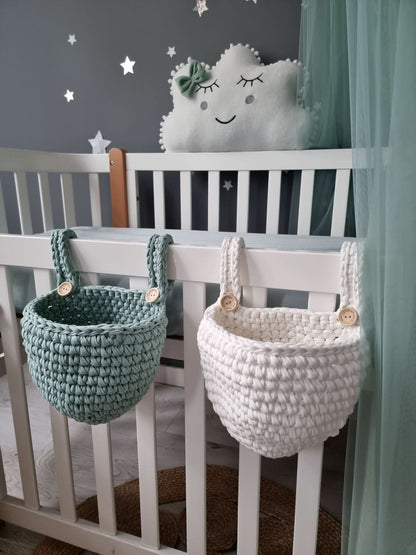 White crib with hanging crochet baskets in a nursery setting