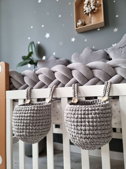 Two gray woven baskets hanging from a white crib with a star-patterned wall in the background.