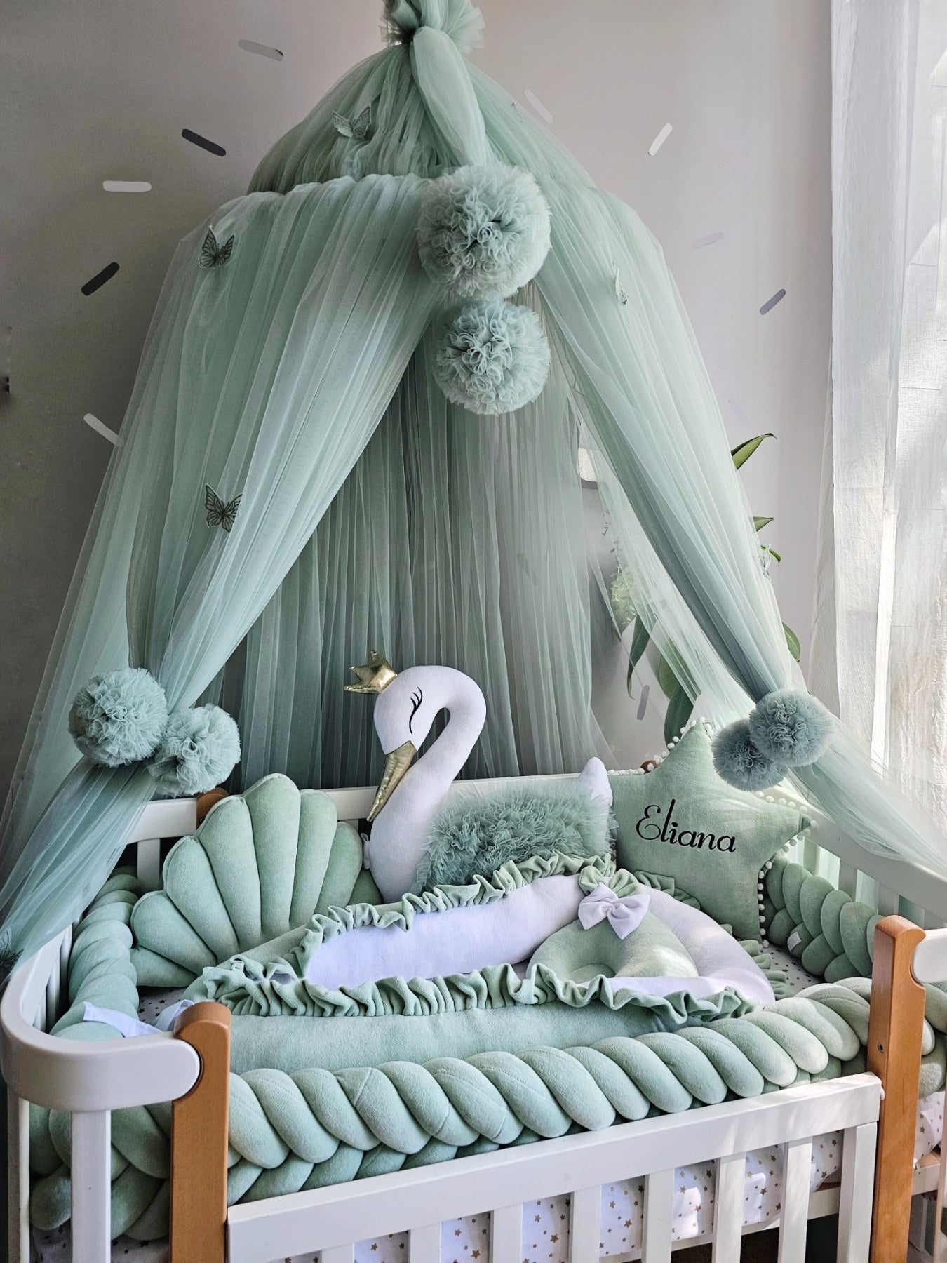 Baby crib with green canopy, swan decoration, and personalized name pillow.