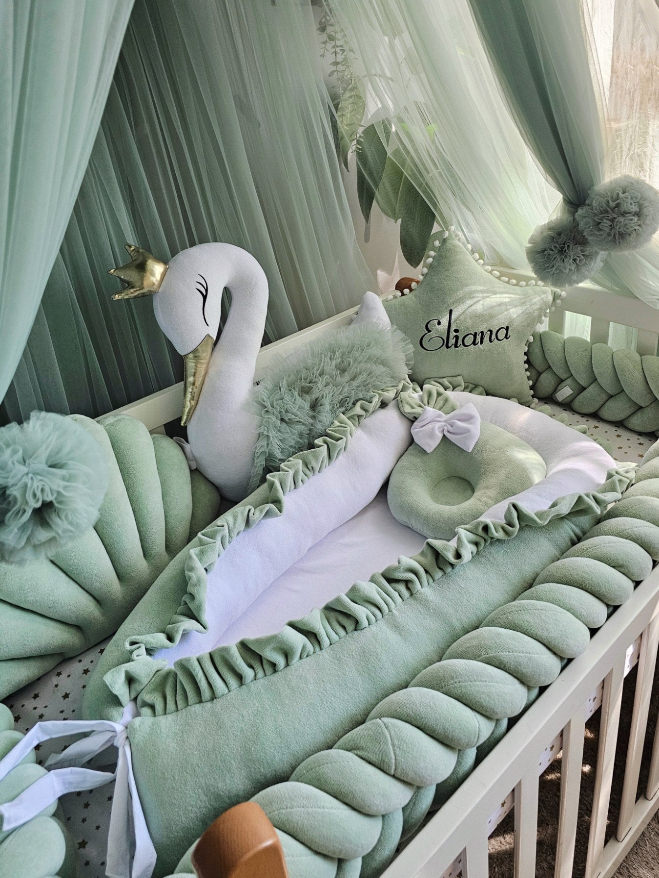 Children's crib with green bedding, swan plush toy, and decorative elements.
