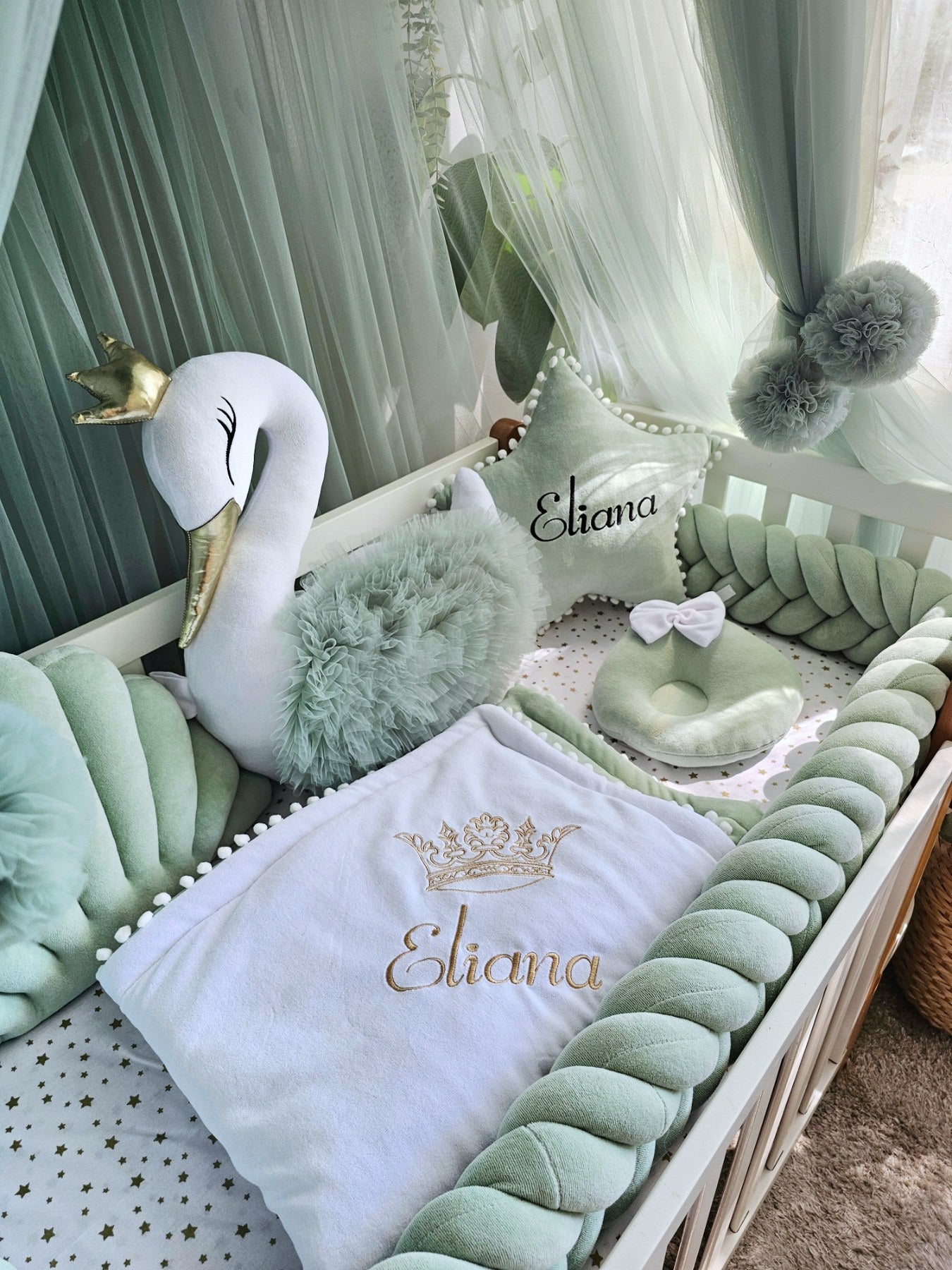 Decorative setup with a plush swan, pillows, and a blanket with baby name  in a nursery.