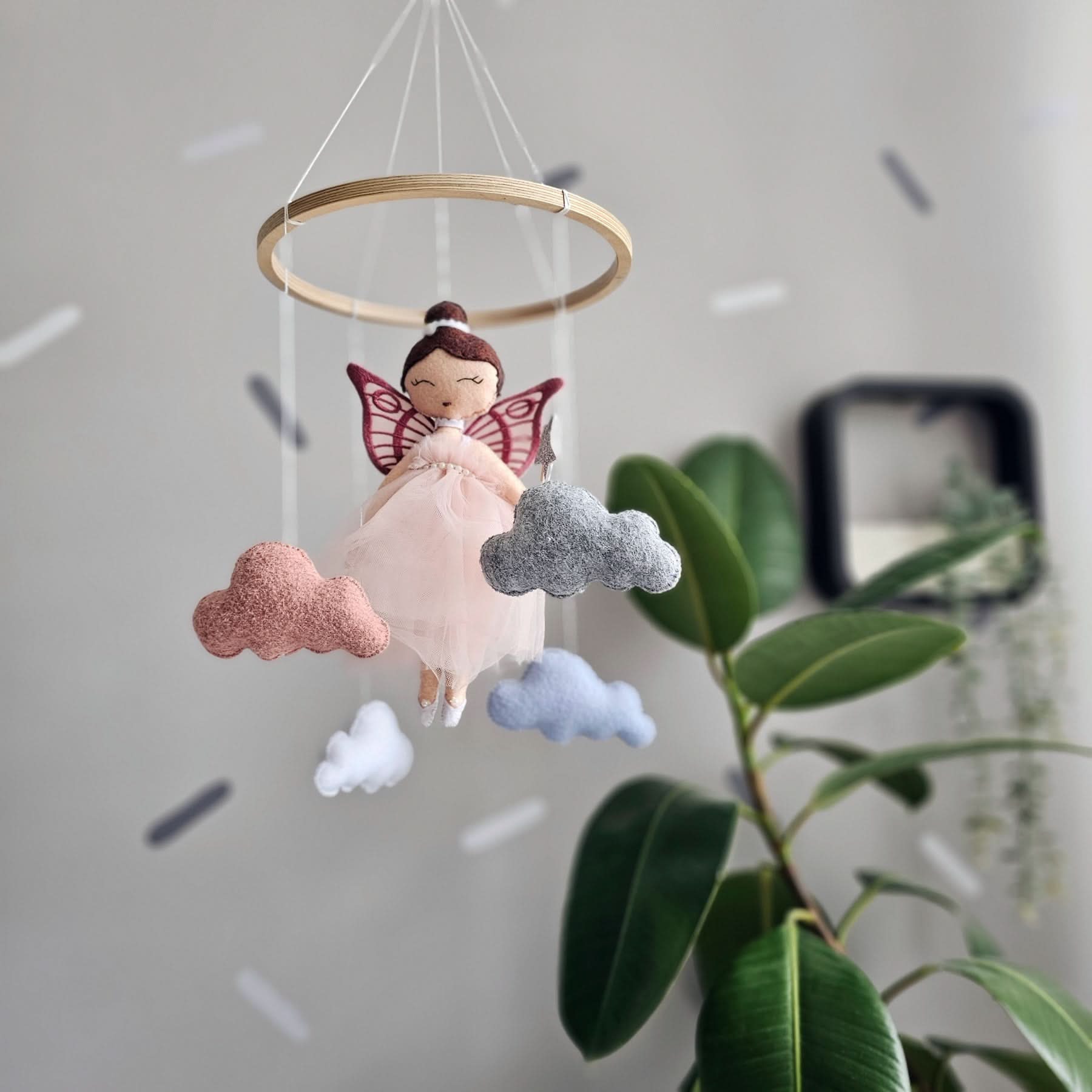 Decorative hanging mobile with fairy and clouds against a neutral background