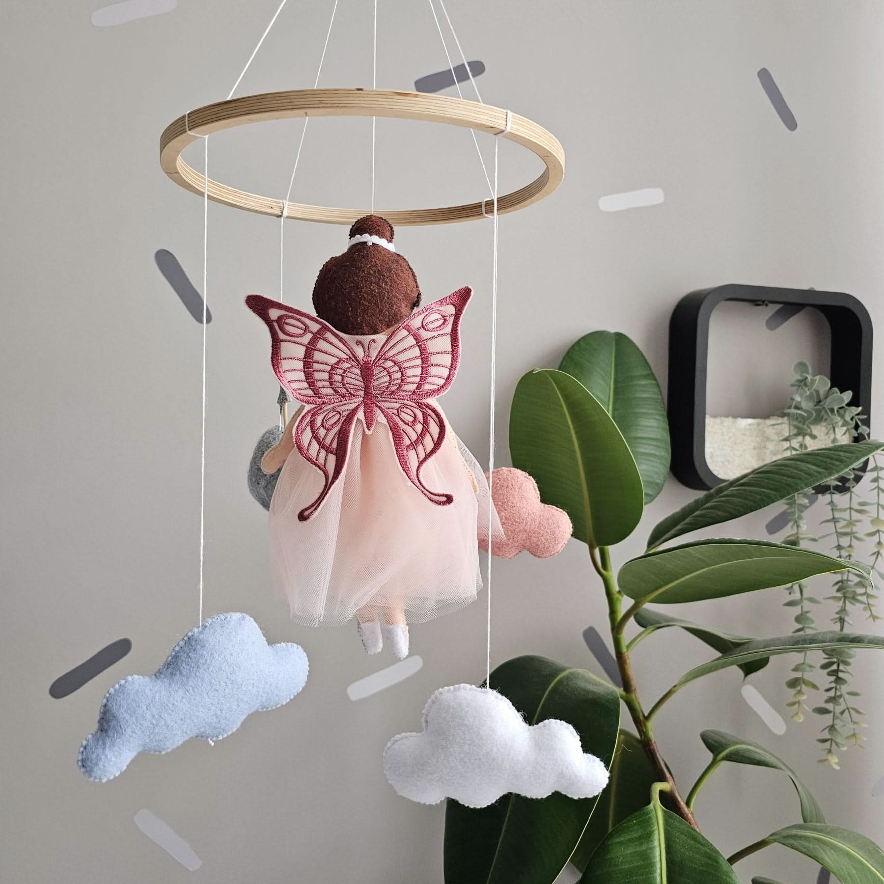 Baby mobile with angel figure and butterfly wings hanging in a room with plants.