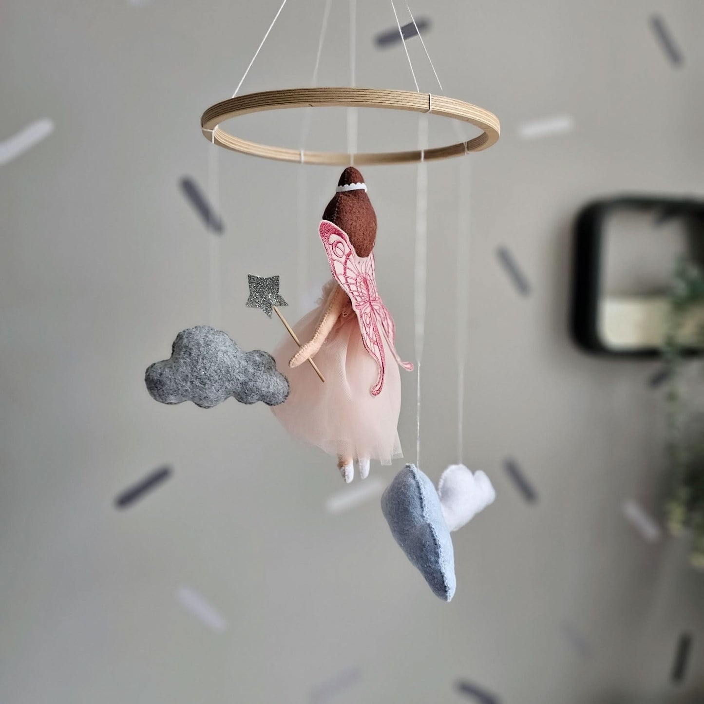 Decorative hanging mobile with angel, cloud, and star shapes against a neutral background