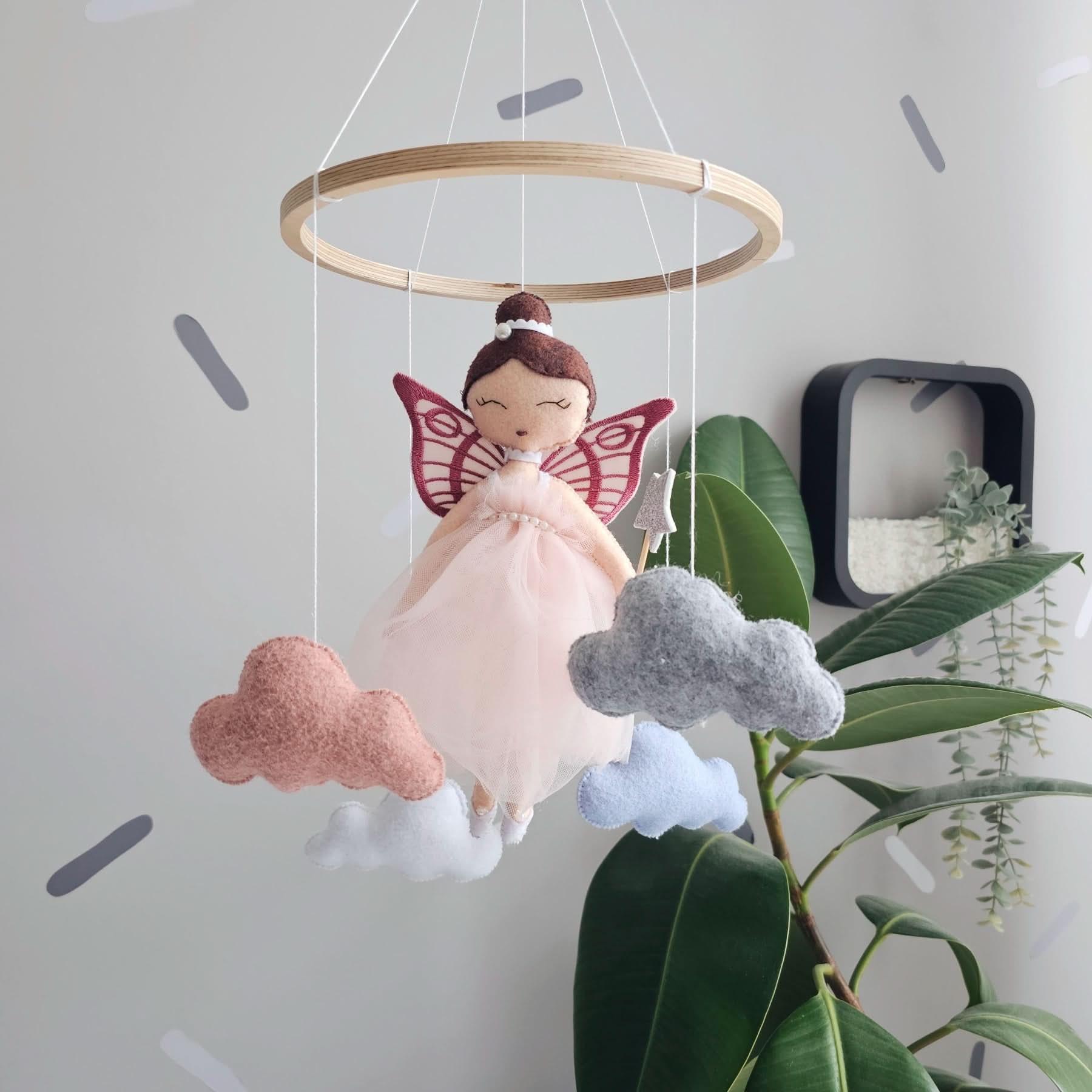 Fairy doll mobile with clouds hanging from a wooden ring against a light gray wall.