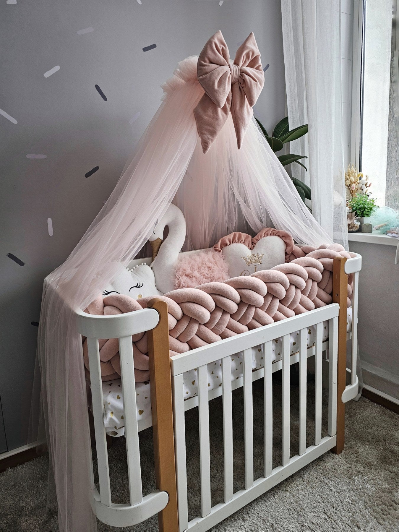Baby crib with pink canopy, swan decor, and soft pillows in a nursery setting.