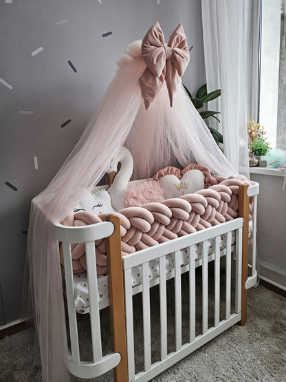 Baby crib with pink canopy, swan decor, and soft pillows in a nursery setting.
