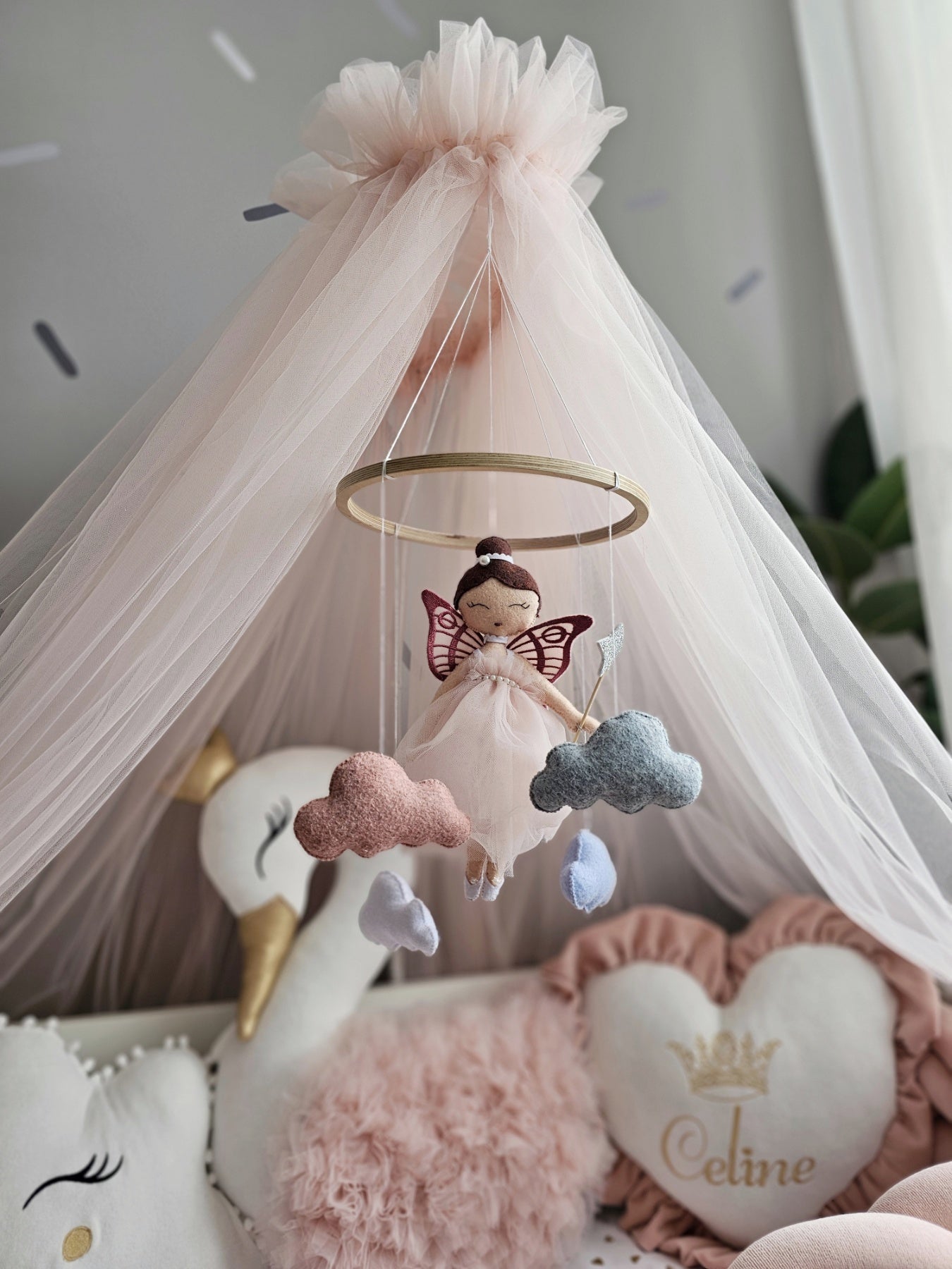 Children's room with pink canopy, fairy mobile, and soft toys.