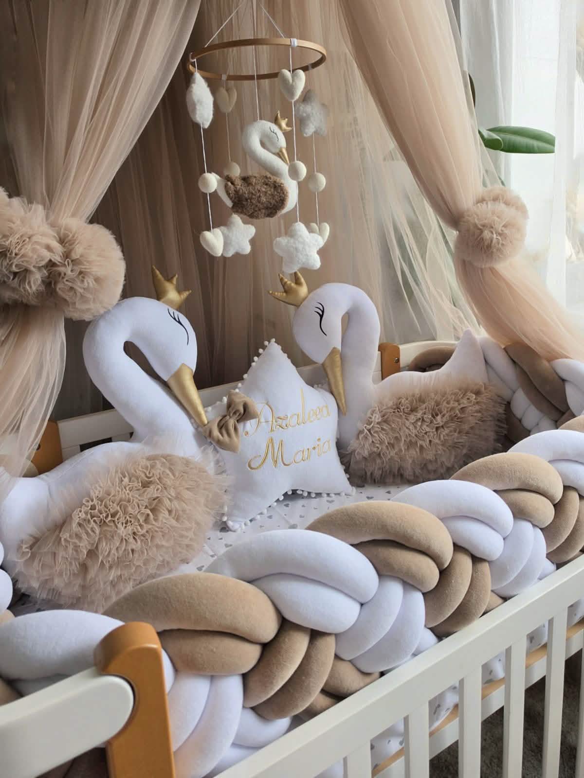 Decorative swan pillows and mobile in a crib with beige and white accents.