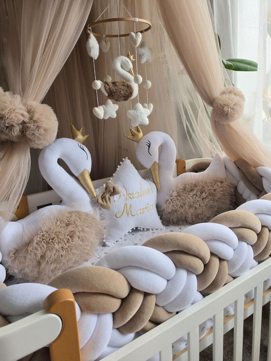 Decorative swan pillows and mobile in a crib with beige and white accents.